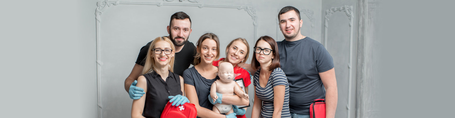A group photo of a young people standing together and holding dummies and emergency kits after the first aid training indoors